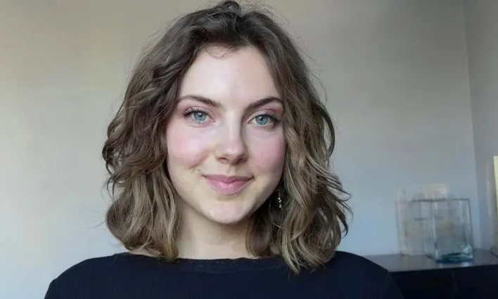Smiling young woman with wavy brown hair and blue eyes in a black top.