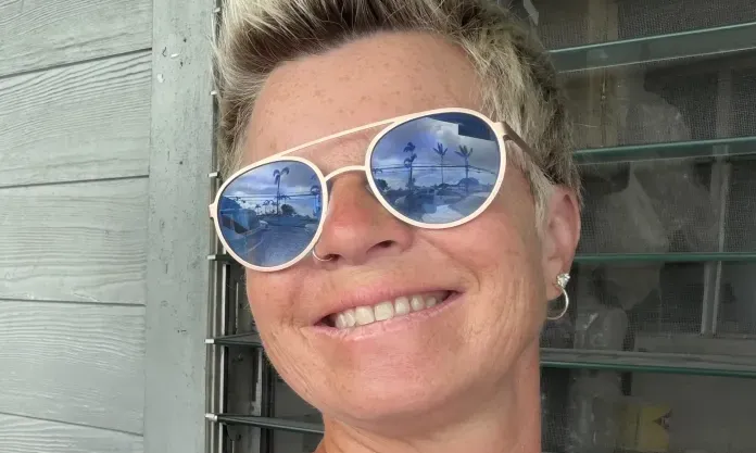 Smiling woman with short blonde hair, wearing reflective sunglasses.