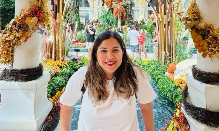 Woman smiles in an indoor garden decorated with autumn leaves and pumpkins.