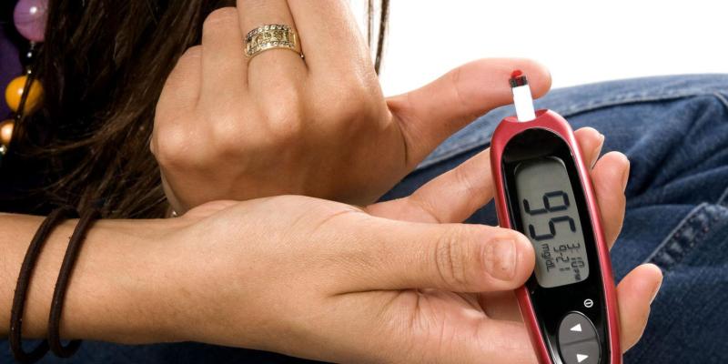 Woman in jeans checking her blood glucose with a red meter