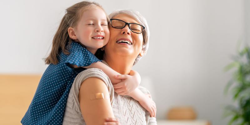 senior woman smiling with a band-aid on her arm and hugging her grandchild
