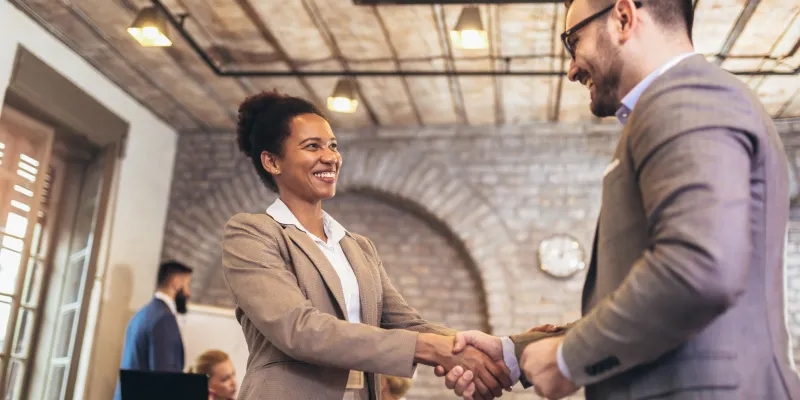 Businesswoman and businessman shaking hands in office setting.