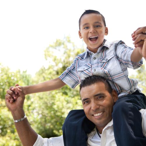 Latinx father with young son on shoulders, smiling