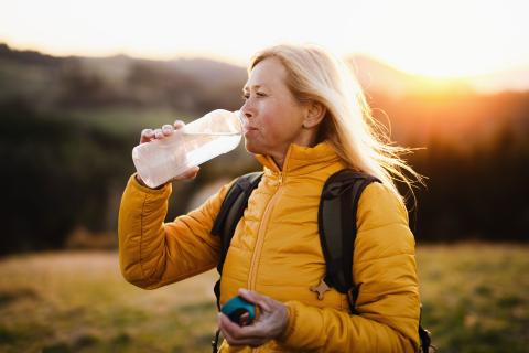 Senior woman walking outdoors drinking from water bottle