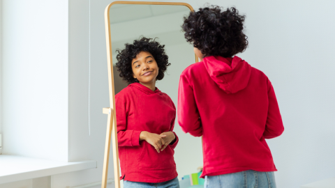 A younger woman looks in the mirror and smiles at herself. 