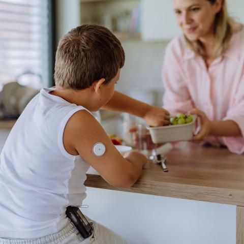 young boy with cgm on arm at kitchen counter with mother eating salad