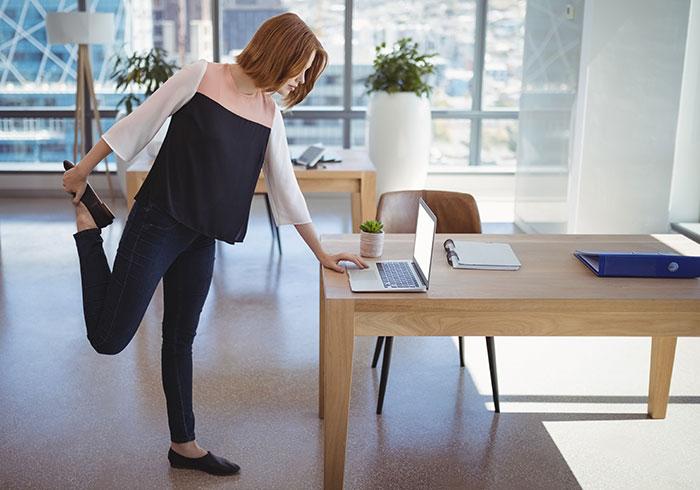 woman-stretching-leg-working-desk-laptop