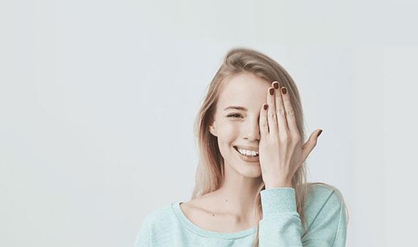 Smiling young woman in light green sweater holding her hand over her eye
