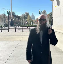 Blind man with beard, sunglasses, and white cane outside the U.S. Capitol.