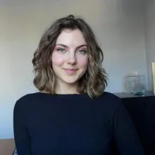 Smiling young woman with wavy brown hair and blue eyes in a black top.