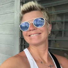 Smiling woman with short blonde hair, wearing reflective sunglasses.