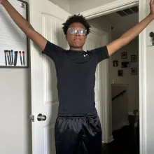Young man in black athletic wear and glasses stands with arms outstretched.