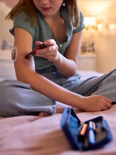 Close Up Of Young girl with Diabetes Sitting On Bed In Bedroom At Home Using Kit To Check Insulin Levels
