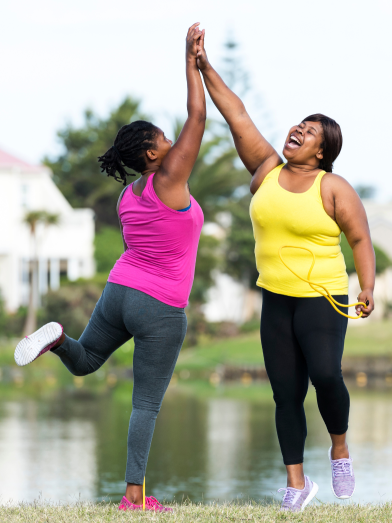 Two women wearing exercise clothes high-five while outside.