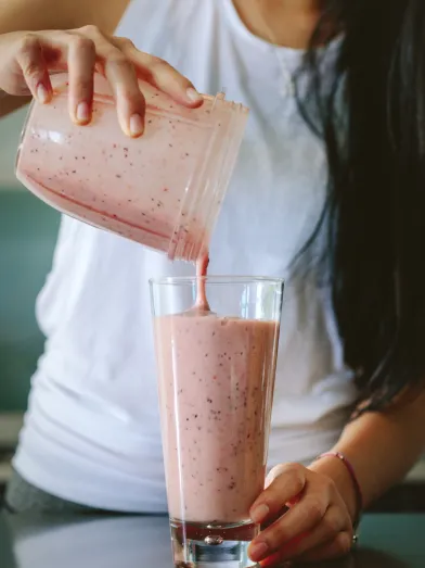 Two hands pour a pink smoothie into a glass.