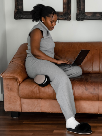 A young Black woman sitting sideways on the couch while looking at laptop