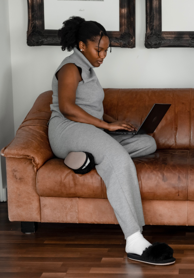 A young Black woman sitting sideways on the couch while looking at laptop