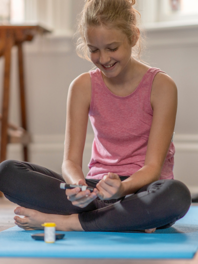 A little girl on a yoga mat is checking her blood glucose level.