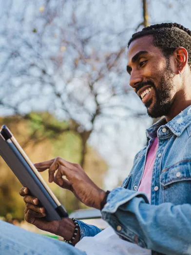 Young African American man on park bench looking at tablet computer screen