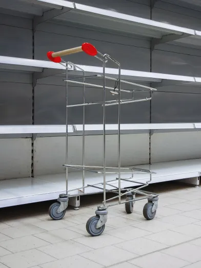 Empty shopping cart in front of empty shelves at supermarket