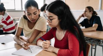 Latina female teacher at desk with Latina teen in school