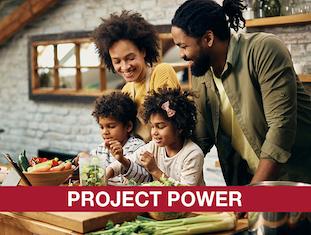 African american husband, wife, and children preparing a meal in the kitchen with Project Power written in white over red banner
